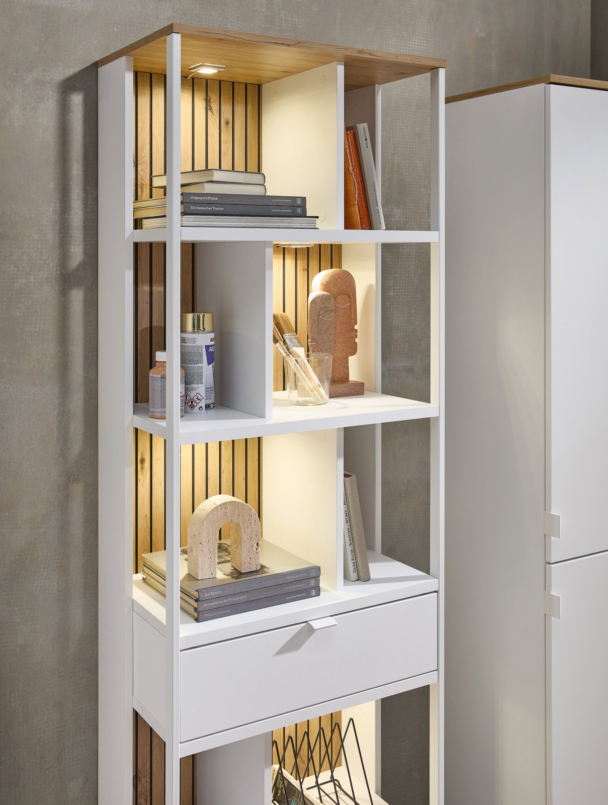 Weißes Büroregal mit mehreren Fächern, dekoriert mit Büchern und Kunstobjekten, aus seitlicher Perspektive fotografiert.
