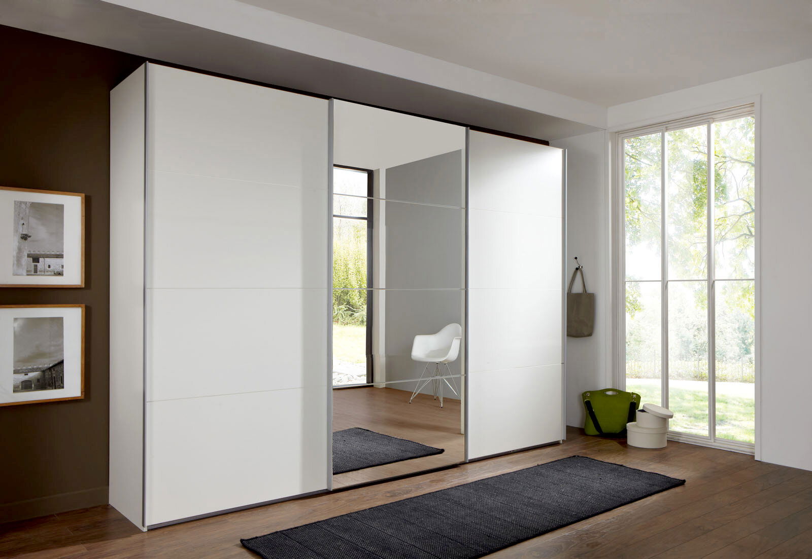 Z2 Schwebetürenschrank 3-türig ERNIE Moderner, dreitüriger Schwebetürenschrank in Weiß mit Spiegel in einem hellen Raum, seitliche Perspektive.