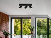 Moderne plafondspot met drie verstelbare lampen in een stijlvolle woonkamer, gezien van onderaf.