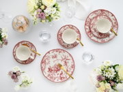 Elegantes Tafelservice mit rot-weiß gemusterten Tellern und Tassen sowie goldfarbenem Besteck auf weißer Tischdecke, dekoriert mit Blumen und Gebäck, fotografiert aus der Vogelperspektive (Top-Down).