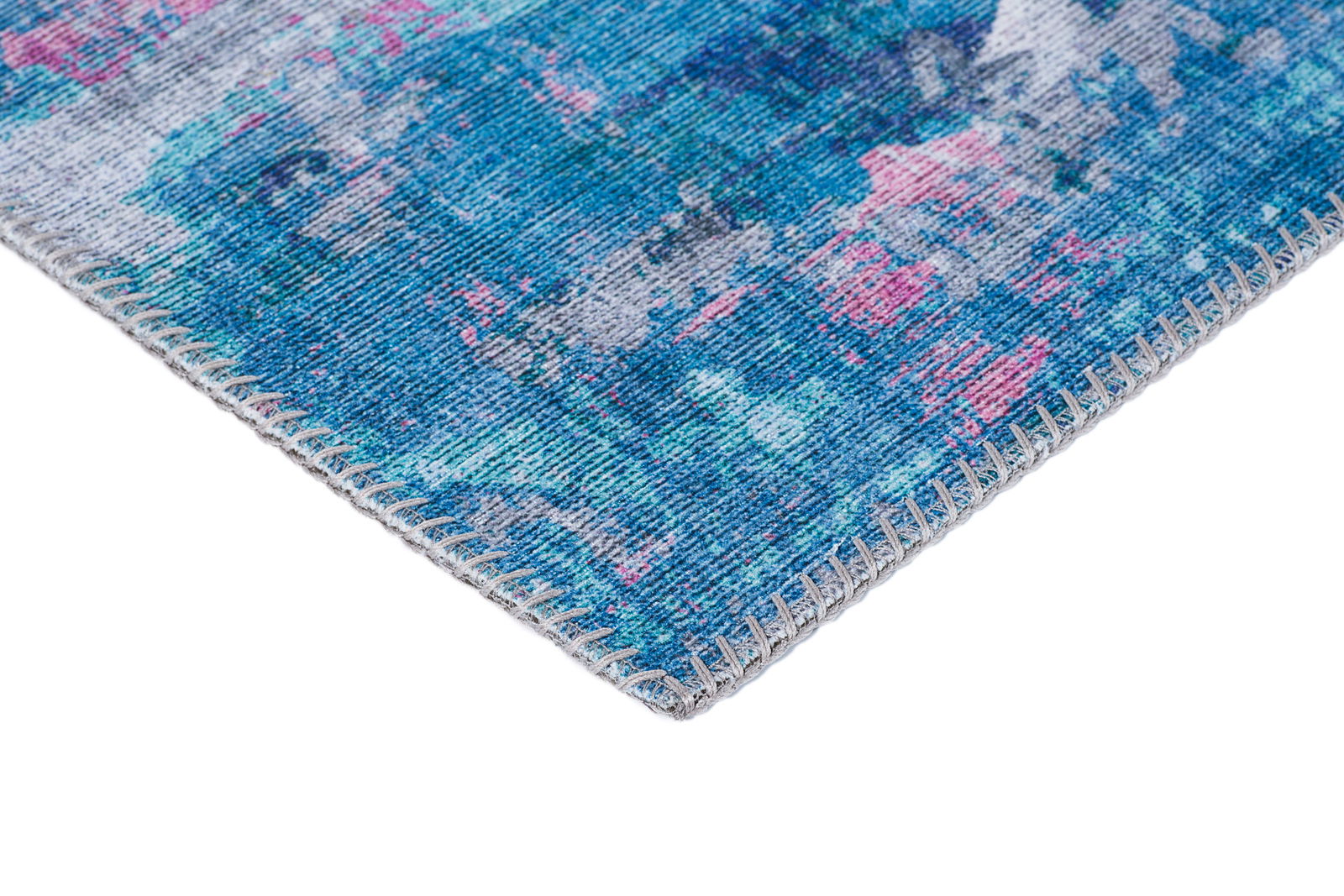 Nahaufnahme einer Ecke eines blauen Teppichs mit rosa und grauen Akzenten, perspektivisch von der Seite aufgenommen.