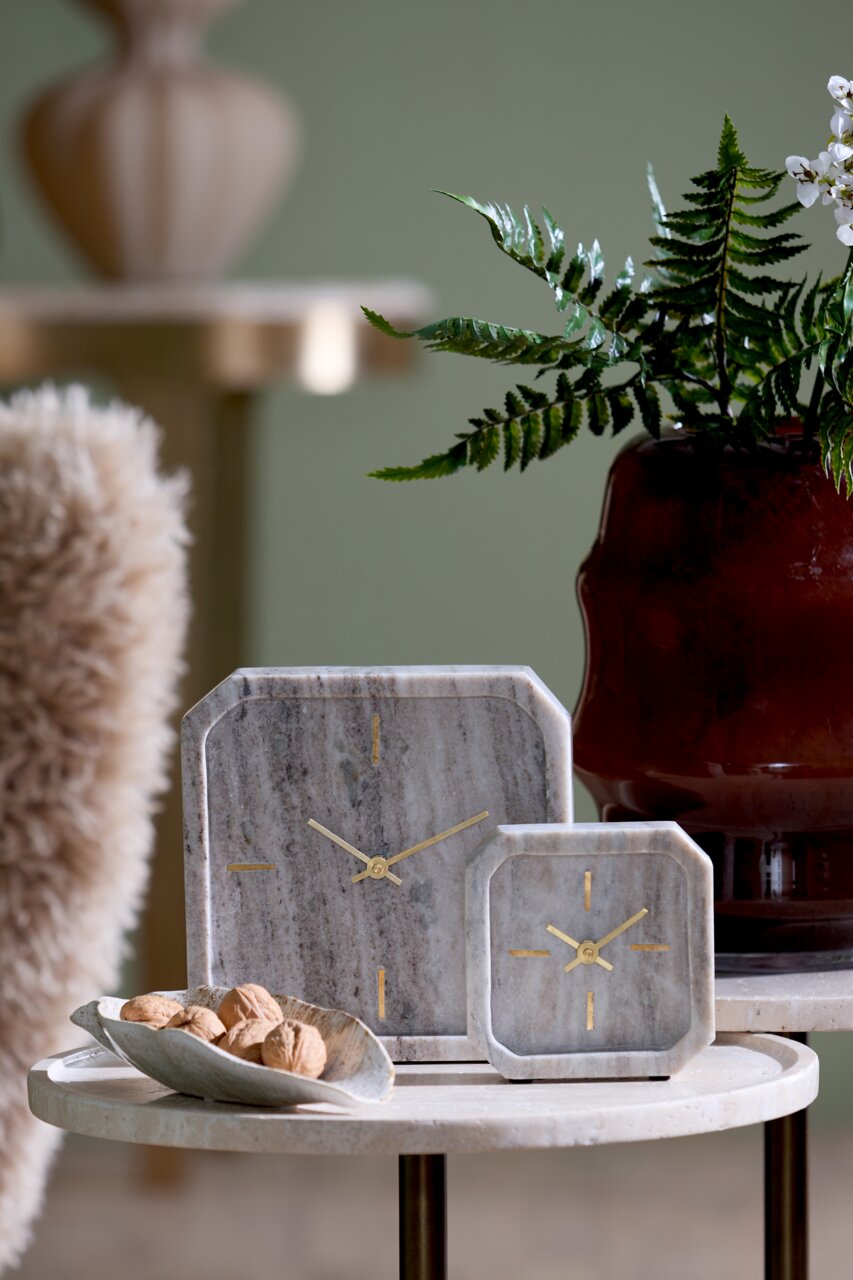 Light&Living Uhr PABLIA Zwei stilvolle Tischuhren aus Marmor mit goldenen Zeigern, auf einem runden Tisch arrangiert, im Hintergrund eine Pflanze und ein dekorativer Topf. Perspektive: Frontalansicht.