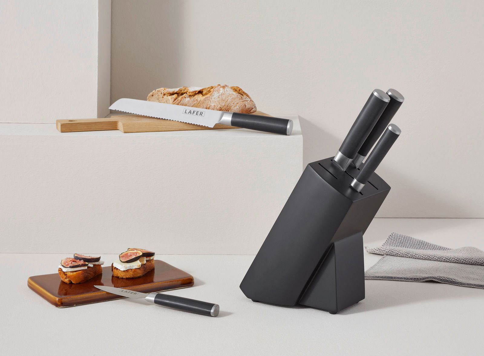 Moderner Messerblock mit sechs Teilen, darunter ein Brotmesser und ein kleines Messer, in einer stilvollen, schwarzen Halterung. Perspektive von vorne rechts.