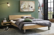 Modernes Holzbett mit schlichtem Kopfteil und Metallfüßen, grau bezogen und mit Kissen dekoriert, im Schlafzimmer-Setting; Perspektive: frontale Seitenansicht leicht von rechts.