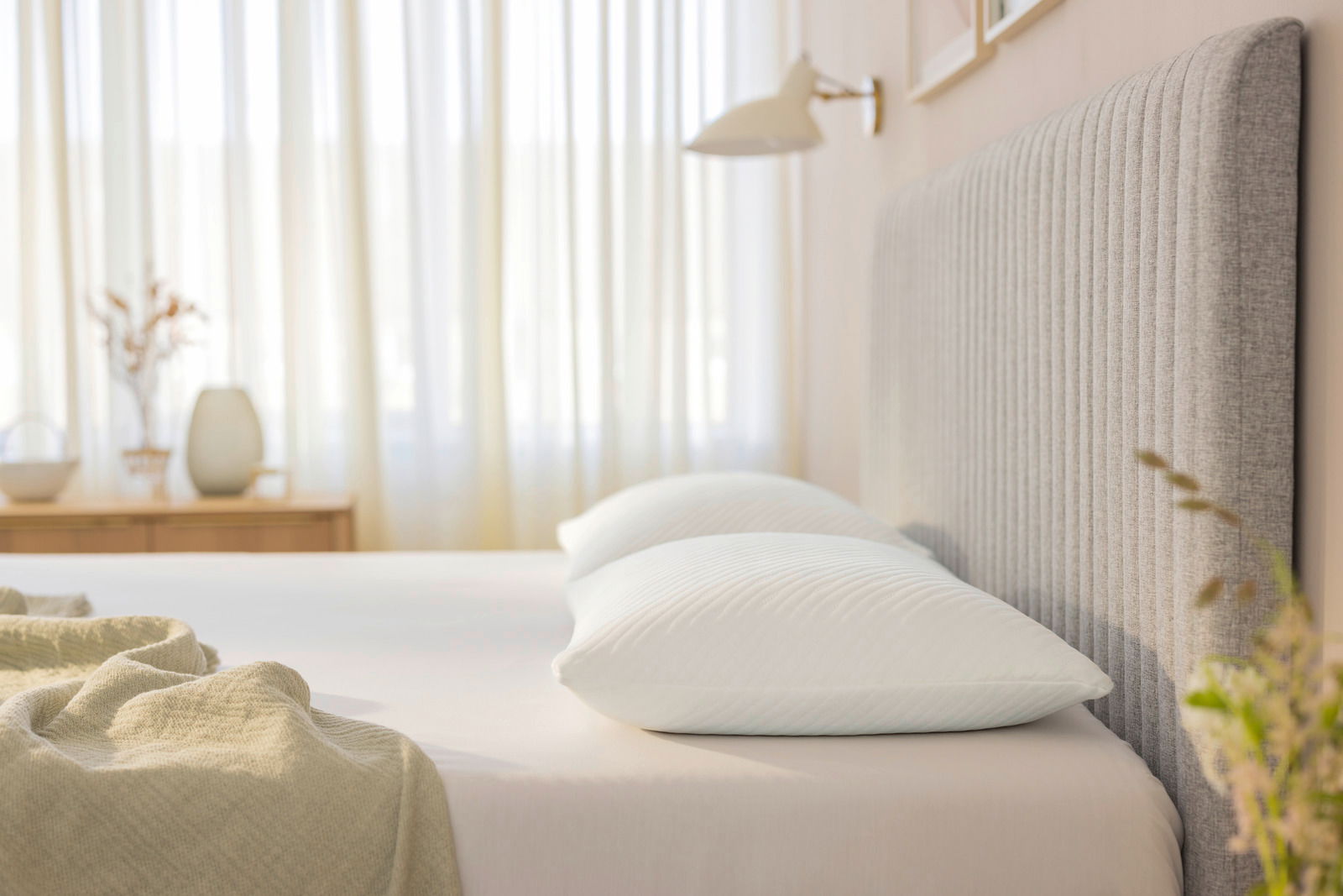 Seitliche Perspektive auf ein Bett mit zwei weißen Schlafkissen, umgeben von einem hellen, gemütlichen Schlafzimmerambiente.