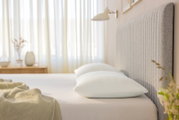 Seitliche Perspektive auf ein Bett mit zwei weißen Schlafkissen, umgeben von einem hellen, gemütlichen Schlafzimmerambiente.