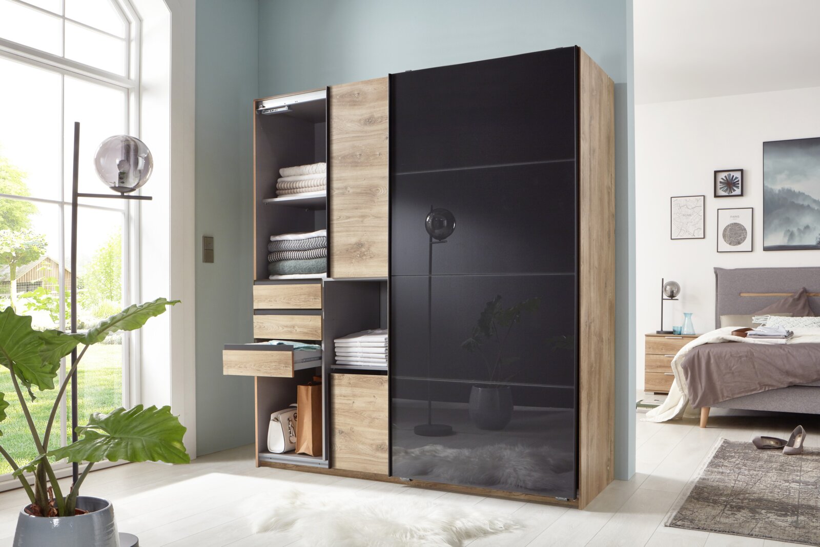 Moderner Schwebetürenschrank mit zwei Türen, links offen mit Regalen und Schubladen, rechts mit schwarzer Front. Perspektive: Frontalansicht im Schlafzimmer.
