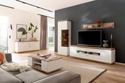 Modernes Wohnzimmer mit weißer Wohnwand in Holzoptik (TV-Lowboard, Vitrine, Sideboard und Couchtisch) vor dunkelgrauer Akzentwand, fotografiert aus leicht erhöhter Front-/Raumperspektive.