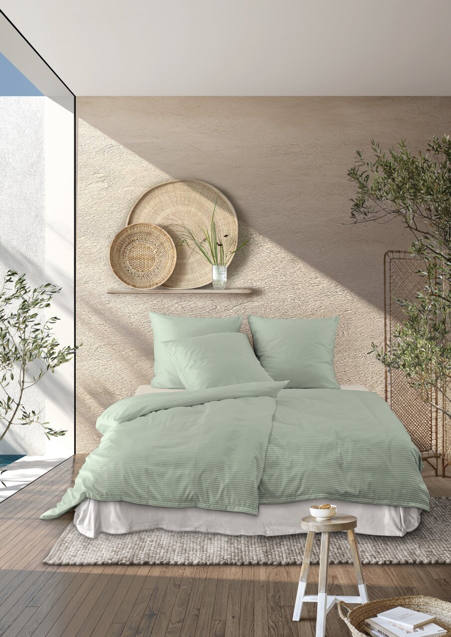 Bettwäsche-Set in sanftem Grün auf einem Bett in einem modern eingerichteten Raum mit Pflanzen und dekorativen Körben an der Wand, aus der Perspektive von vorne betrachtet.