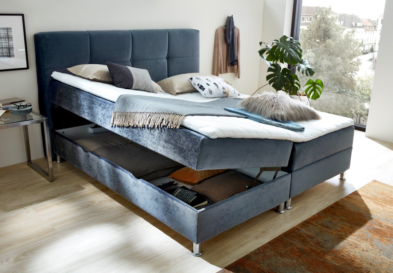 Boxbett mit Stauraum, seitliche Perspektive, dekoriert mit Kissen und Decken, in einem modernen Schlafzimmer mit großem Fenster.