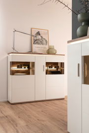 Modernes Highboard in Weiß mit Holzdetails, dekoriert mit einer Lampe und einem Glasgefäß, seitliche Perspektive