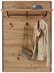 Garderobenpaneel aus Holz mit Haken und Ablage, frontal fotografiert. Auf der Ablage liegen ein Hut und ein Korb, an den Haken hängen eine Jacke und eine Tasche.