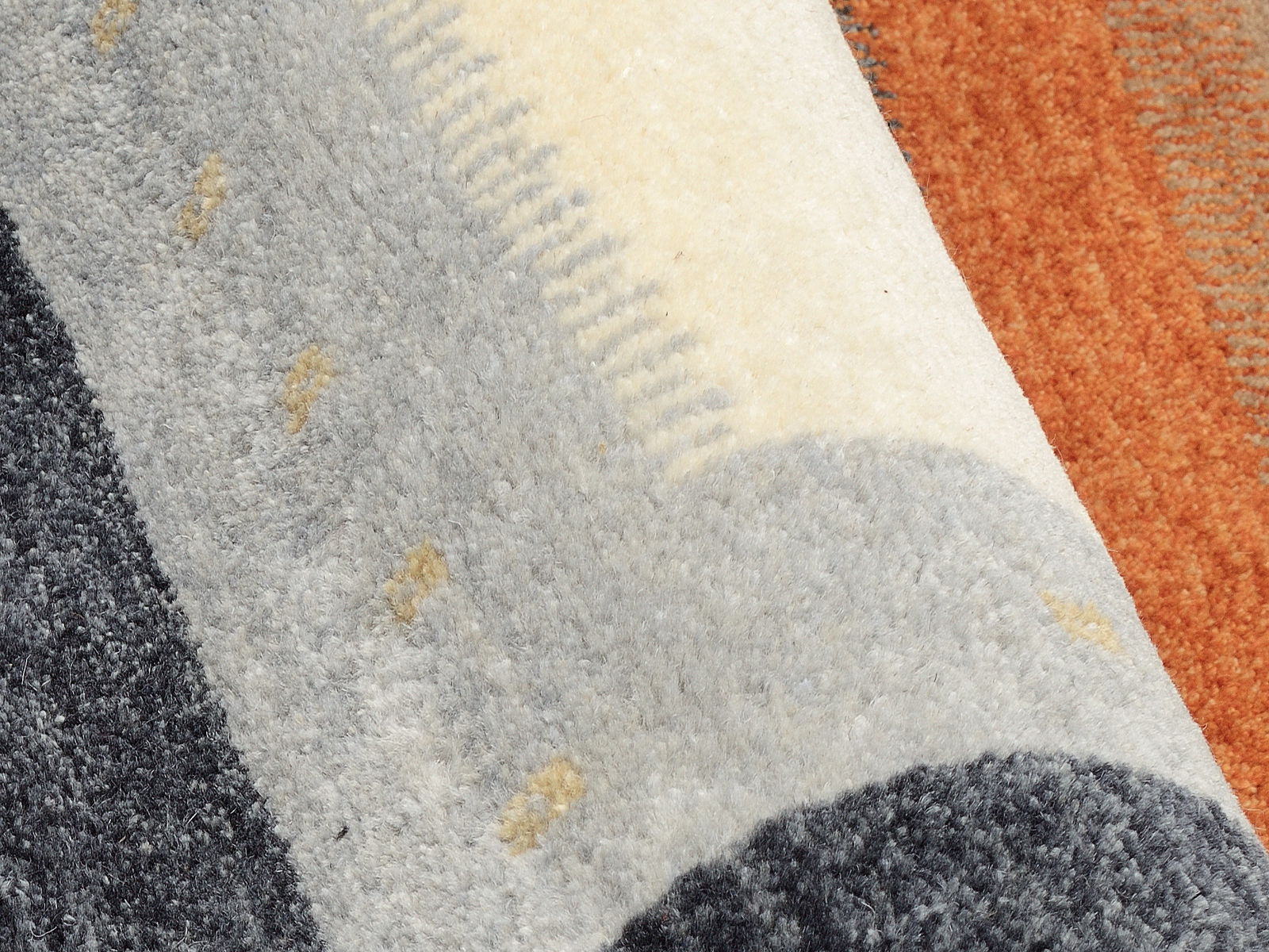 Nahaufnahme eines Wollteppichs mit grauen, weißen und orangefarbenen Streifen, diagonale Perspektive