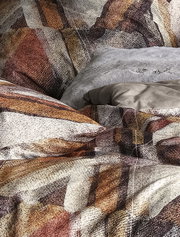 Nahaufnahme einer Bettwäsche mit abstraktem Muster in Erdtönen, Perspektive von oben.