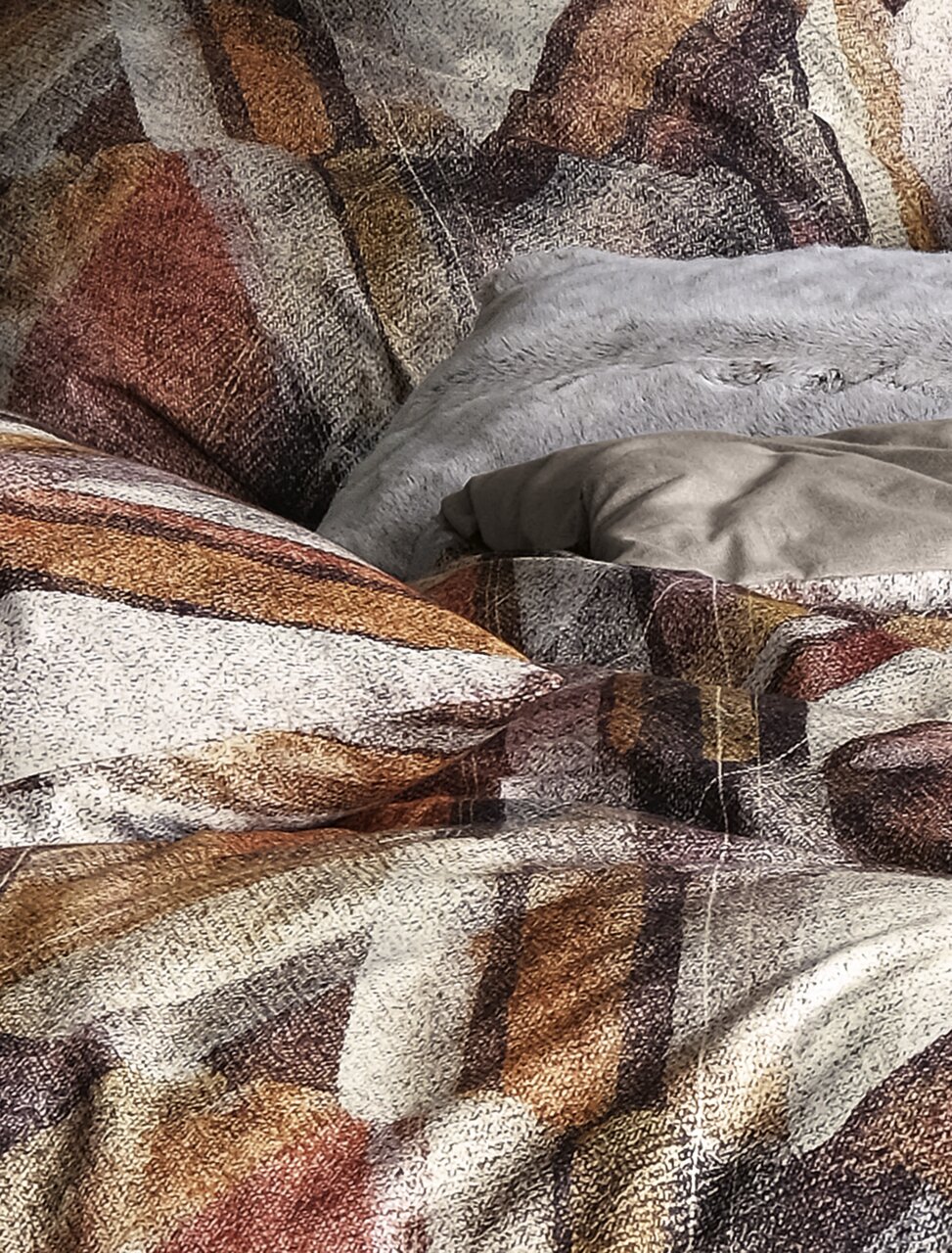 Nahaufnahme einer Bettwäsche mit abstraktem Muster in Erdtönen, Perspektive von oben.