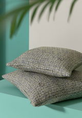 Zwei übereinander gestapelte Zierkissenhüllen mit strukturierter Oberfläche in Grün- und Grautönen, seitliche Perspektive.