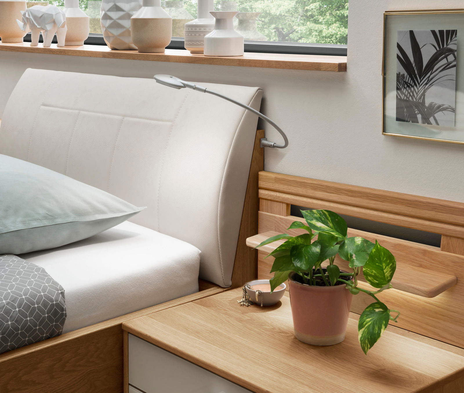Komfortbett mit gepolstertem Kopfteil in Seitenansicht, dekoriert mit Pflanzen und modernen Accessoires.