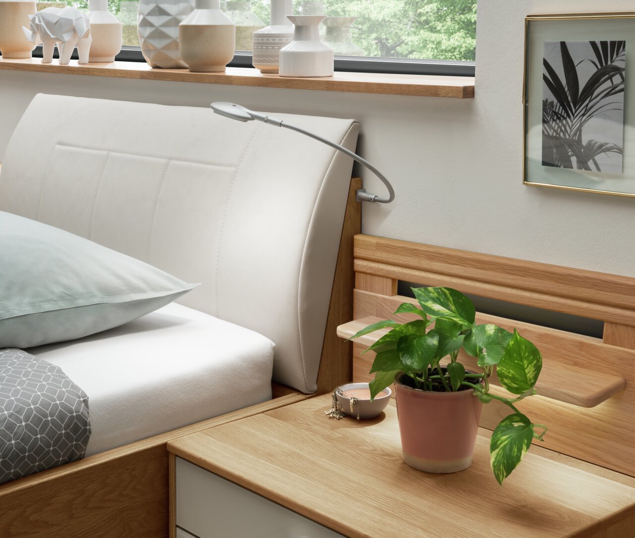 Comfortabel bed met gestoffeerd hoofdeinde, gezien vanaf de zijkant, versierd met planten en moderne accessoires.