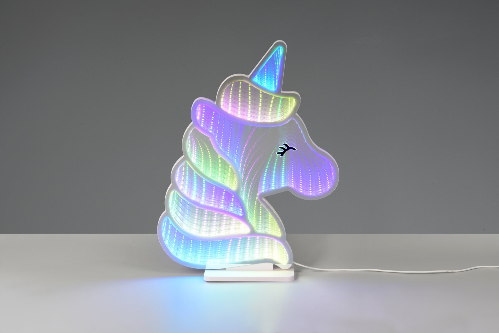 Bunte LED-Dekoleuchte in Einhorn-Kopf-Form mit Regenbogen-Lichteffekt auf weißem Sockel, Frontansicht auf grauem Hintergrund
