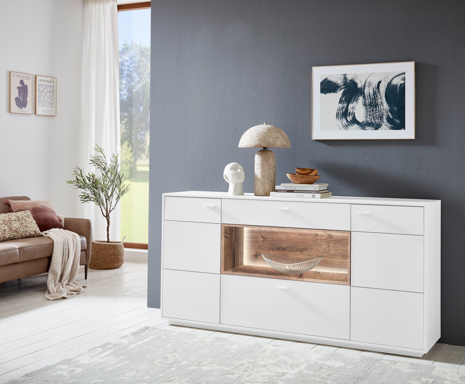 Weißes Sideboard mit Holzdetails, dekoriert mit Büchern und Skulpturen, in einem modernen Wohnzimmer. Frontalansicht.