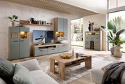 Moderne wandmeubel in een lichte woonkamer met grote ramen, bestaande uit verschillende kasten en een tv-meubel in houtlook met grijze fronten, gezien vanaf de zijkant.