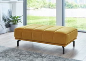Gelber XXL-Hocker in modernem Wohnzimmer, seitliche Perspektive mit Blick auf große Fenster und grüne Landschaft im Hintergrund.