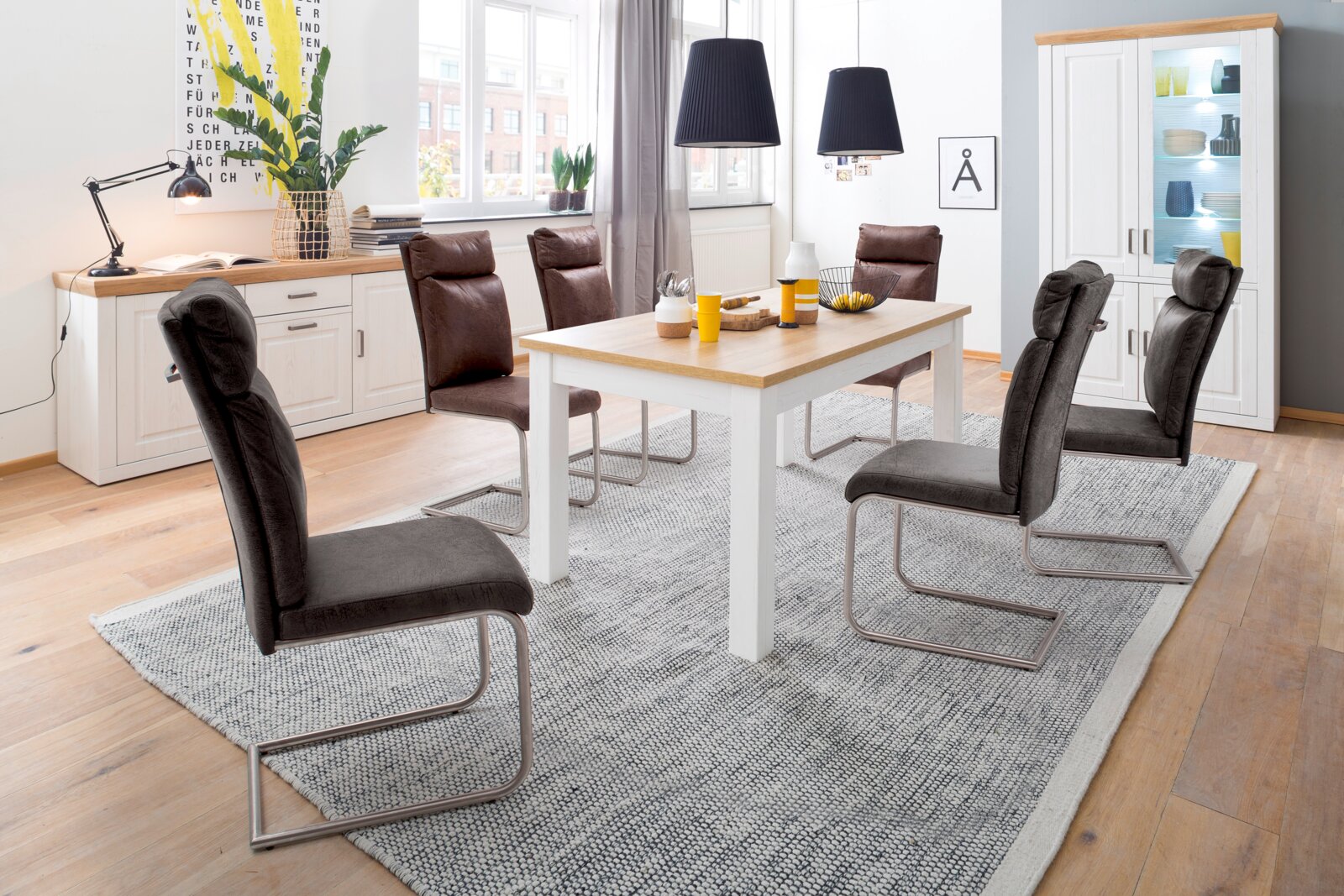 Modernes Esszimmer mit weißem Esstisch mit Holzplatte, vier gepolsterten Freischwinger-Stühlen in Dunkelgrau/Braun, Sideboard und Vitrine; Aufnahme in leicht erhöhter, schräger Frontperspektive.