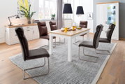 Modernes Esszimmer mit weißem Esstisch mit Holzplatte, vier gepolsterten Freischwinger-Stühlen in Dunkelgrau/Braun, Sideboard und Vitrine; Aufnahme in leicht erhöhter, schräger Frontperspektive.
