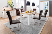 Modernes Esszimmer mit weißem Esstisch mit Holzplatte, vier gepolsterten Freischwinger-Stühlen in Dunkelgrau/Braun, Sideboard und Vitrine; Aufnahme in leicht erhöhter, schräger Frontperspektive.