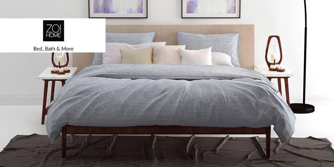 Ein gemütliches Bett mit hellgrauer Bettwäsche, vielen Kissen und zwei Nachttischen mit Lampen.