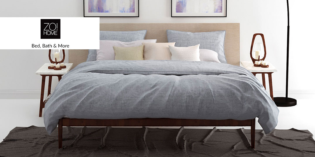 Een knus bed met lichtgrijs beddengoed, veel kussens en twee nachtkastjes met lampjes.