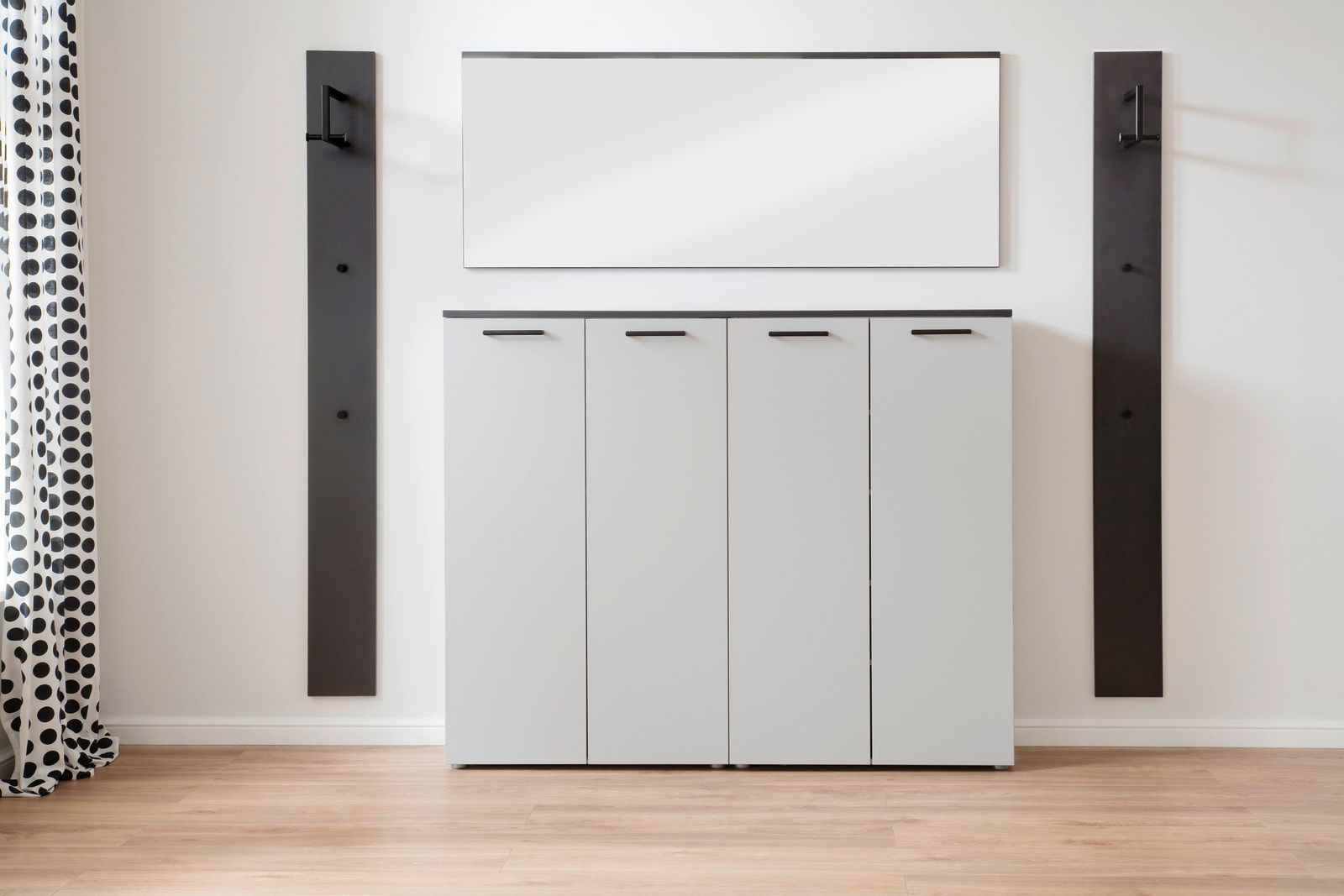 Moderne Garderobenkombination mit vier weißen Schranktüren, zwei schwarzen Wandpaneelen und einem rechteckigen Spiegel, frontal betrachtet.