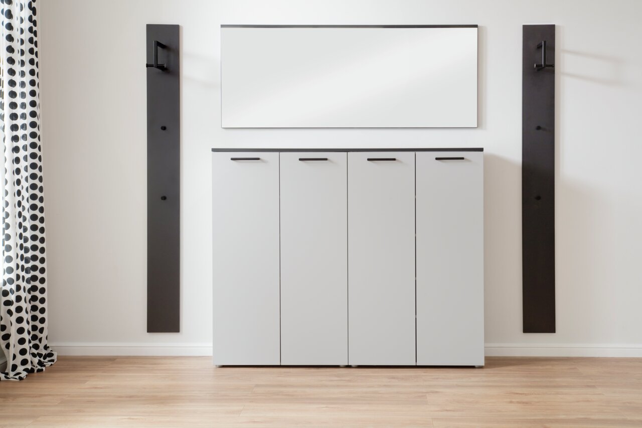 Moderne Garderobenkombination mit vier weißen Schranktüren, zwei schwarzen Wandpaneelen und einem rechteckigen Spiegel, frontal betrachtet.
