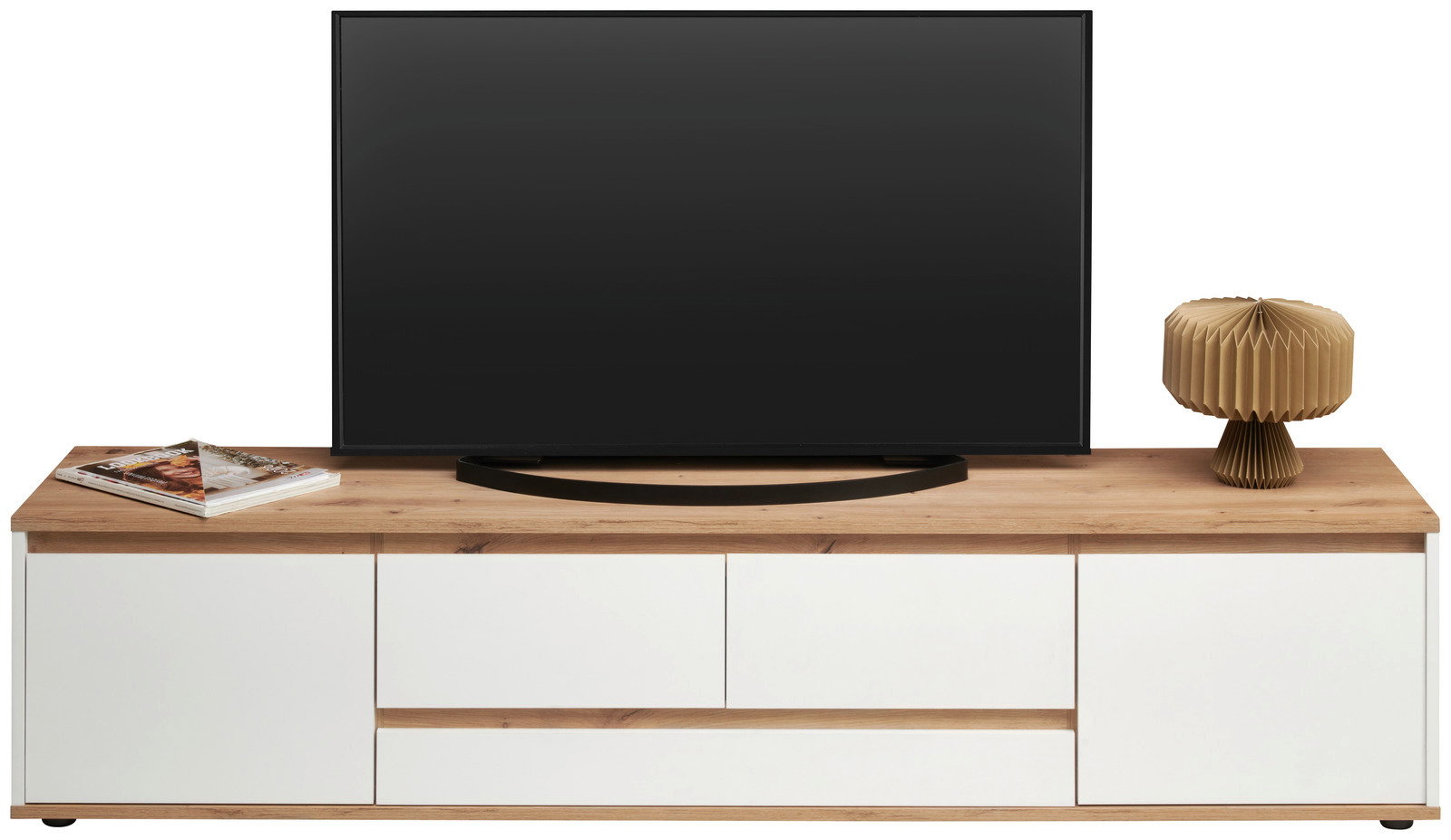 Frontansicht eines XL-TV-Lowboards mit Holzoberfläche, weißem Korpus, einem Fernseher, einer Lampe und Zeitschriften.