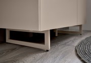 Detailaufnahme aus niedriger Perspektive: weißer Badezimmerschrank/Waschtischunterschrank mit offenem Metallgestell und schwarzen Füßen auf grauem Holzfußboden neben rundem Teppich