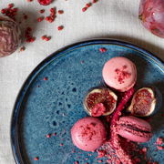 Vogelperspektive auf einen blauen Teller mit feinem Muster, dekoriert mit rosa Macarons, frischen Feigen und roten Beeren.