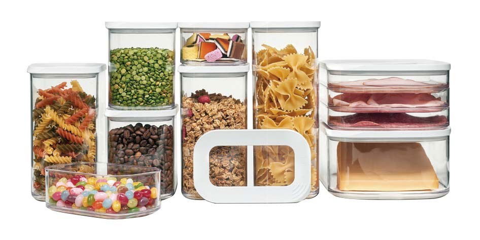 Vorratsdosen-Set aus transparentem Kunststoff mit weißen Deckeln, gefüllt mit verschiedenen Lebensmitteln wie Nudeln, Bohnen, Süßigkeiten und Aufschnitt, frontal betrachtet.