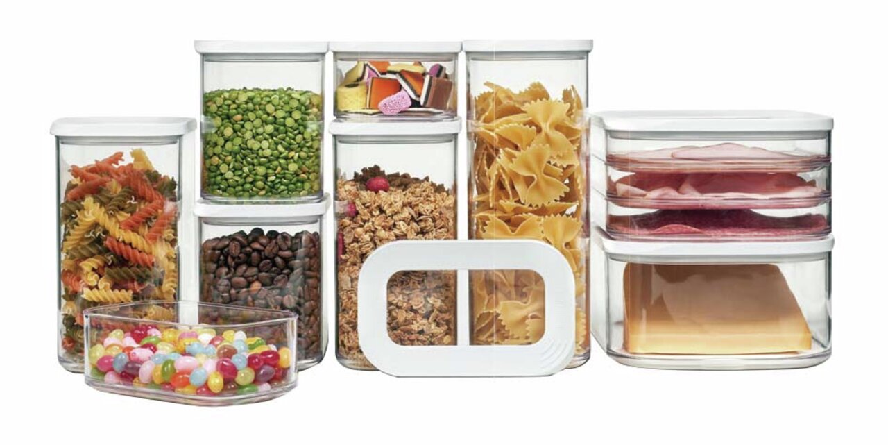 Set voorraadbussen van doorzichtig kunststof met witte deksels, gevuld met diverse levensmiddelen zoals pasta, bonen, snoep en vleeswaren, gezien vanaf de voorkant.