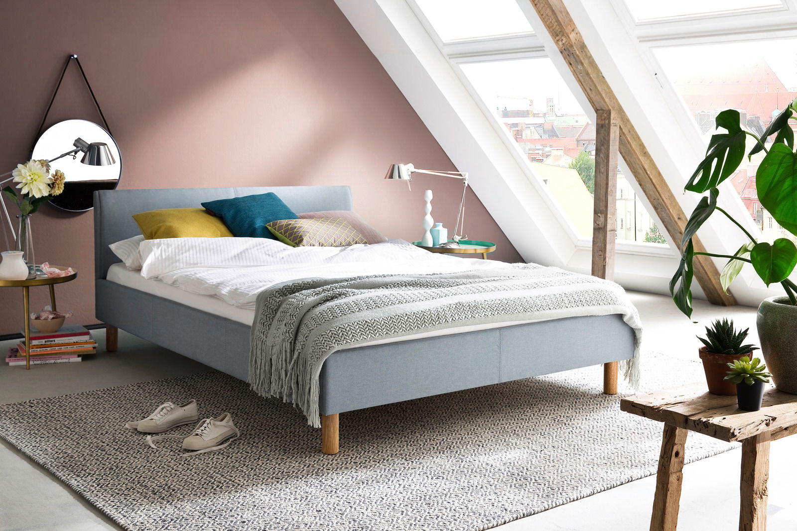 Modernes Polsterbett in einem stilvollen Dachgeschosszimmer mit schrägen Fenstern, seitliche Perspektive.