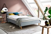 Modern gestoffeerd bed in een stijlvolle zolderkamer met schuine ramen, zijaanzicht.