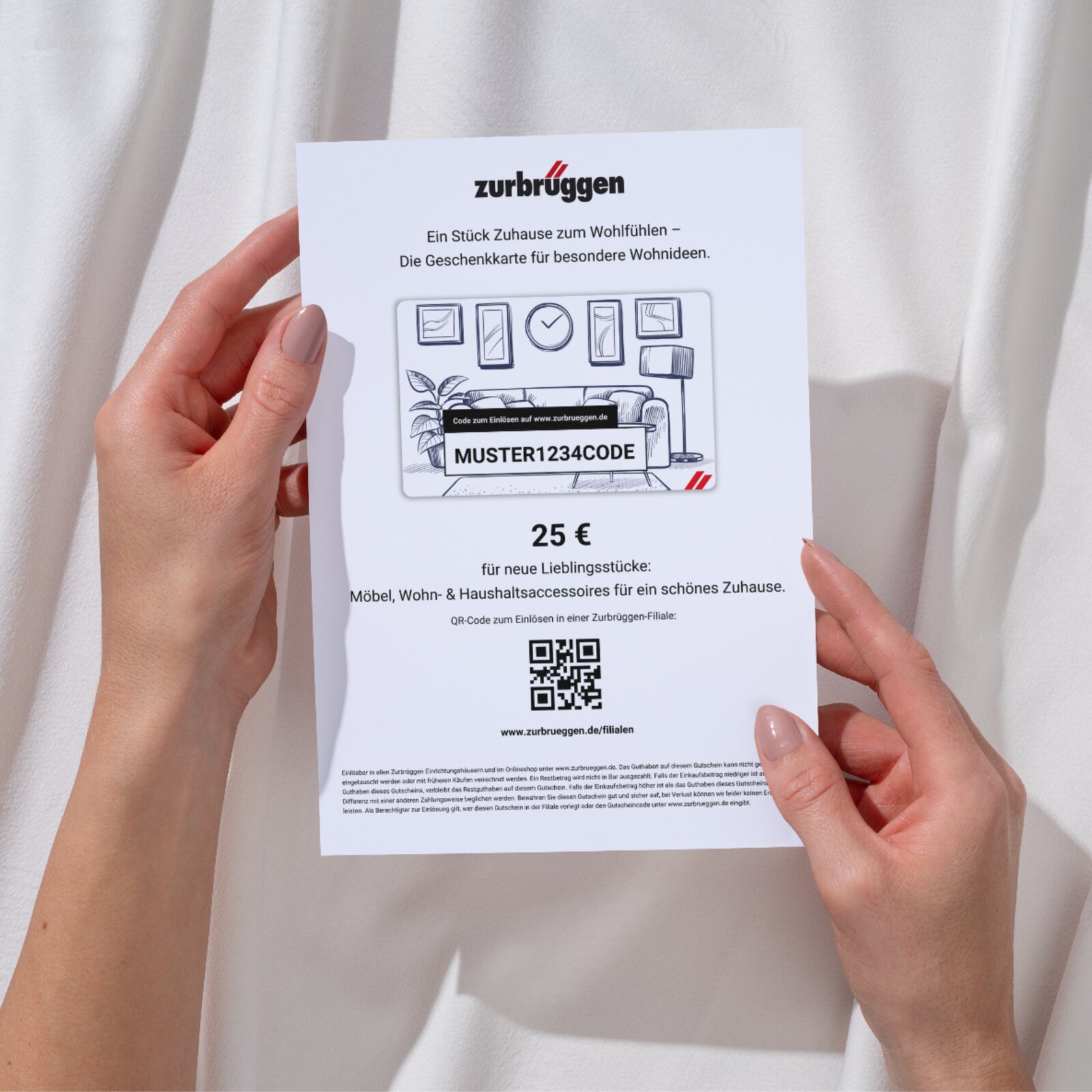 Twee handen houden een Zurbrüggen-cadeaubon ter waarde van 25 euro vast, gefotografeerd vanuit vogelperspectief. Op de bon staat een woonkamerontwerp afgebeeld en er staat een QR-code op om de bon in te wisselen.