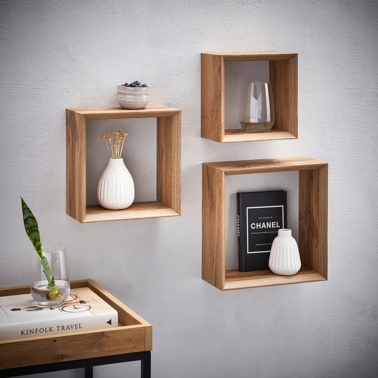 Dreiteiliges Wandregal-Set aus Holz in quadratischer Form, an einer weißen Wand montiert, mit dekorativen Objekten wie Vasen und Büchern, aus einer frontalen Perspektive betrachtet.