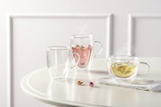Drie dubbelwandige kopjes op een tafel, twee gevuld met thee en één leeg, gefotografeerd vanuit een zijaanzicht.