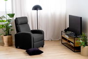 Modernes Wohnzimmer mit einem TV-Lowboard aus Holz und Metall, seitliche Perspektive. Daneben ein schwarzer Fernseher, eine Stehlampe und ein grauer Sessel. Pflanzen und Dekorationen ergänzen das gemütliche Ambiente.