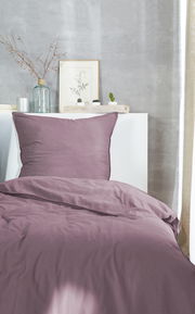 Lila Bettwäsche-Set auf einem Bett, frontal fotografiert, mit dekorativen Elementen im Hintergrund.