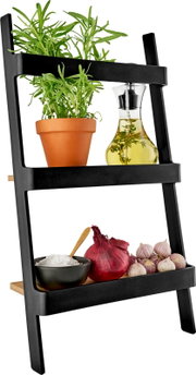 Schuin zijaanzicht van een zwart, laddervormig keukenrek met houten plankjes, met een rozemarijnplant in terracotta pot, een glazen oliefles met kruiden, een schaaltje zout met lepel, een rode ui en knoflook op een witte achtergrond.