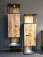 Zwei moderne Stand-/Hängeelemente aus Holz mit Metallrahmen, frontal fotografiert. Die Schränke haben eine natürliche Holzmaserung und integrierte Beleuchtung.