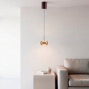 Moderne Pendelleuchte mit zylindrischem Deckenbaldachin und getöntem Glas-Lampenschirm, warm leuchtend über einem minimalistischen Wohnzimmer mit Sofa und Beistelltisch, Frontalansicht leicht von unten