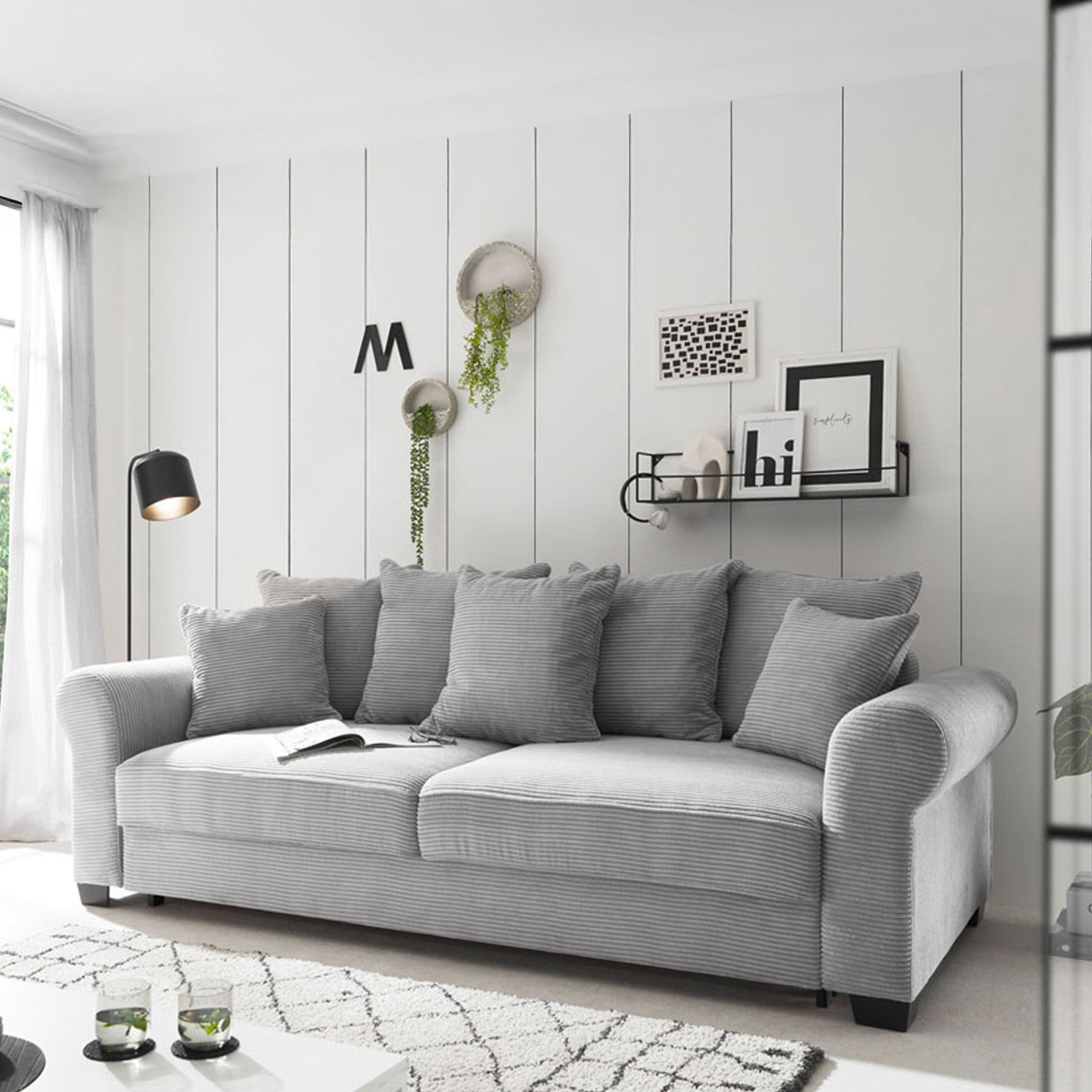 Modernes graues 3-Sitzer-Sofa mit Cordbezug und Kissen vor weißer Wandpaneel-Optik im skandinavischen Wohnzimmer.