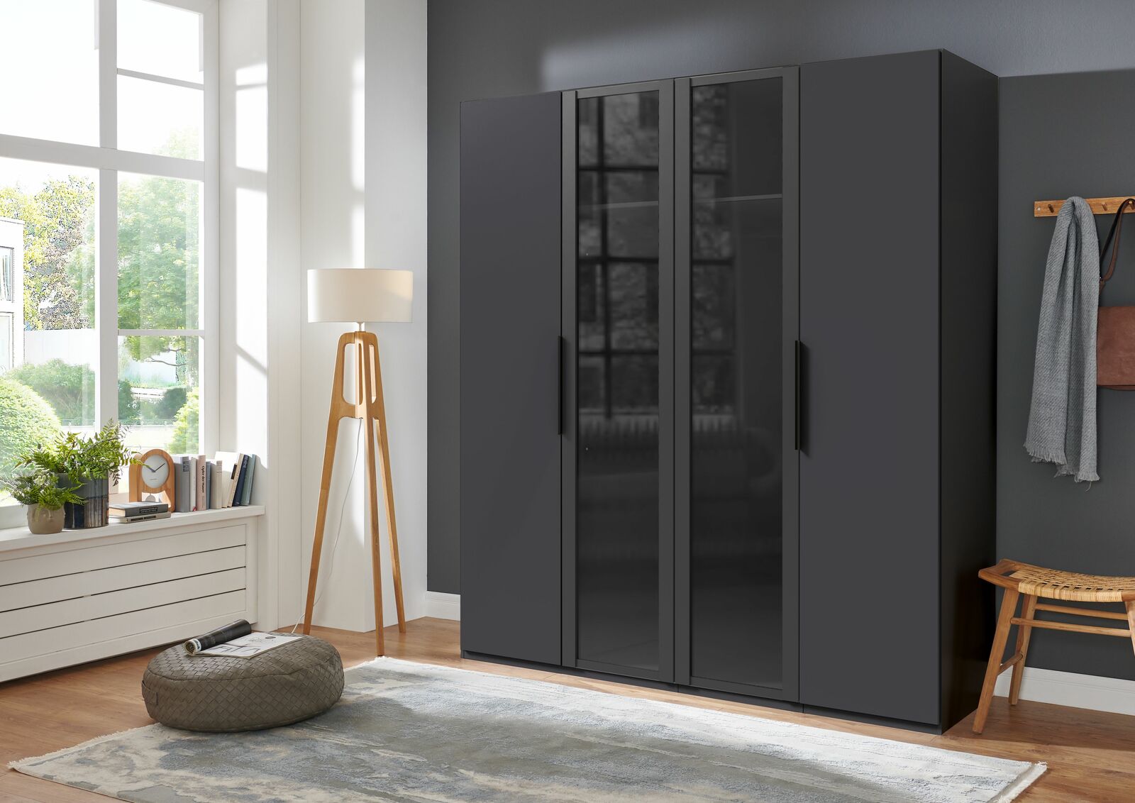 Moderner, schwarzer Drehtürenschrank mit vier Türen, frontal fotografiert in einem stilvoll eingerichteten Raum mit großen Fenstern.